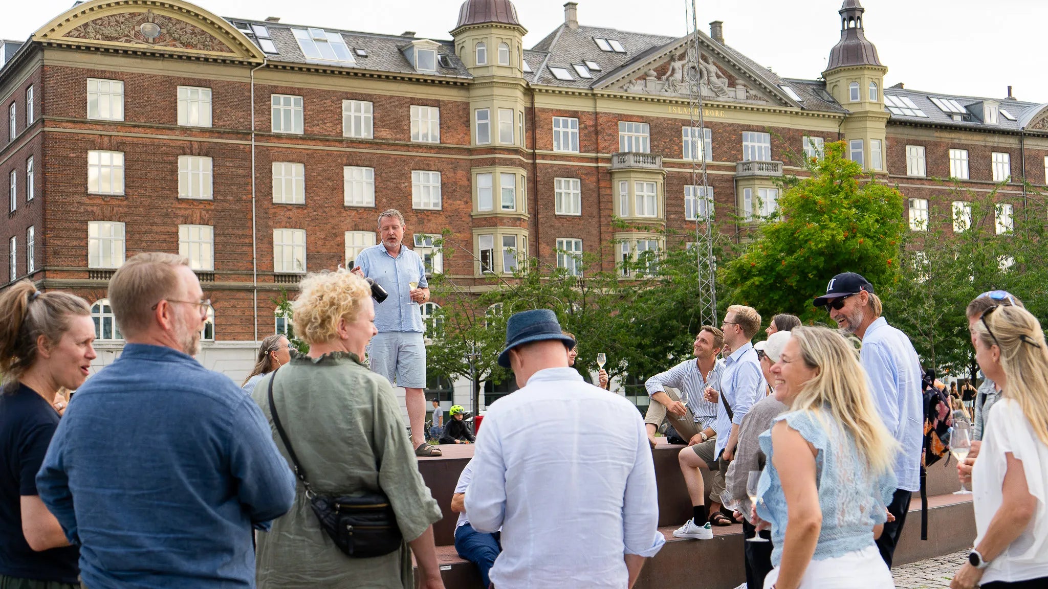 Mikkel står og fortæller noget sjovt om champagne, og får en menneskemængde til at grine